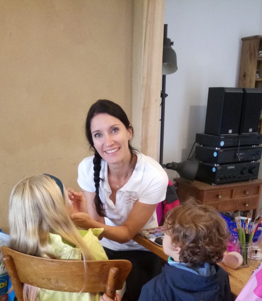Frau schminkt Kinder am Tisch