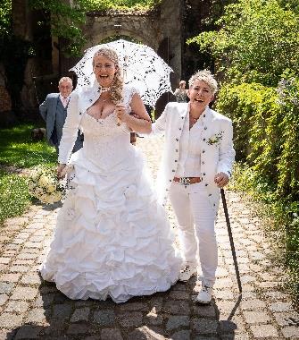 Zwei lachende Bräute
in Weiß gehen
glücklich über einen
gepflasterten Weg und
genießen ihren
Hochzeitstag.