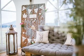 Gemütliche Lounge-Ecke
mit Palettensofa, Kissen
und einer dekorierten
Holzwand für eine Auszeit
während der Feier.